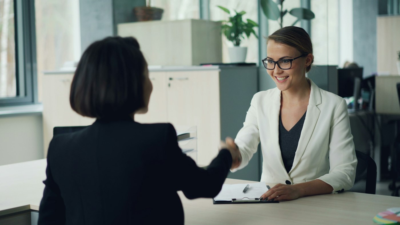 🎬 FULL 4K VIDEO for this still is in my bio link! ⬇️ Good-looking young lady from human resources department is interviewing a female professional shaking hands then asking questions and writing. Employment and successful youth concept.